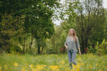 A young blonde woman plays badminton on a lawn in a park.