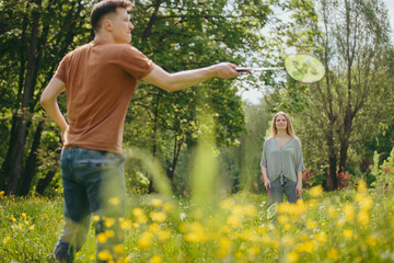 A young man and his girlfriend spend time together playing badminton on a lawn in a park.