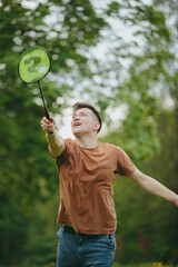 Close-up of a young man playing badminton on a lawn in a park.