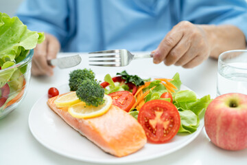 Asian elderly woman patient eating salmon steak breakfast with vegetable healthy food in hospital.