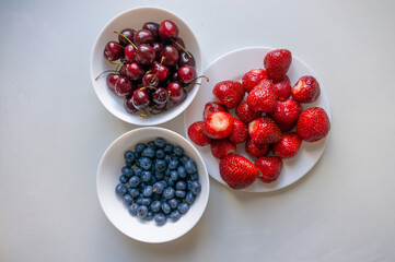 Top view of whole blueberry, cherry in a bowl and strawberry on a plate