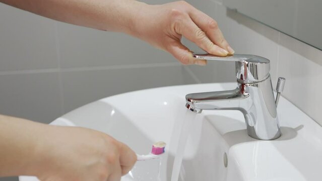 Woman's hands, toothbrush and person at tap for water,dental hygiene and gum care at home.Brushing teeth and rinse oral product for fresh grooming,morning routine at bathroom sink.Water saving concept