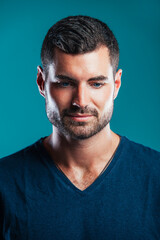 Fototapeta premium Closeup portrait of stylish handsome bearded man looking down, in studio isolated over turquoise background. Vertical portrait.