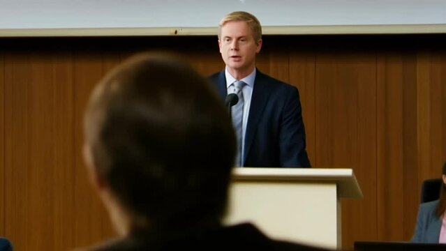 Caucasian male speaker at a conference podium addressing an audience. Concept of public speaking, business presentation, corporate event, professional seminar.