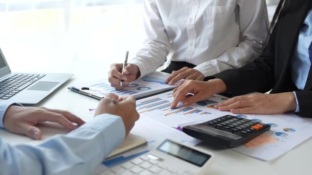 Professionals collaborate on financial analysis, reviewing charts and graphs, using calculators and laptops to discuss data and strategy