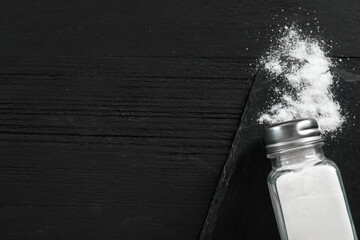 Salt shaker on black wooden table, top view. Space for text