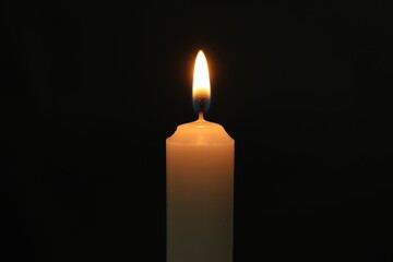 One burning church candle on black background, closeup