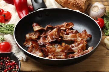 Delicious bacon slices in frying pan and products on wooden table, closeup