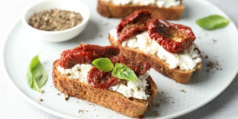Delicious ricotta bruschettas with sun dried tomatoes, basil and milled pepper on light table, closeup