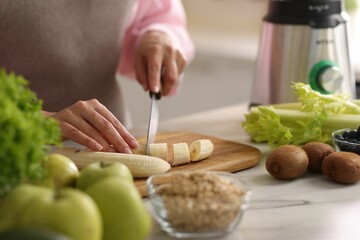 Woman cutting banana for smoothie at white marble table in kitchen, closeup