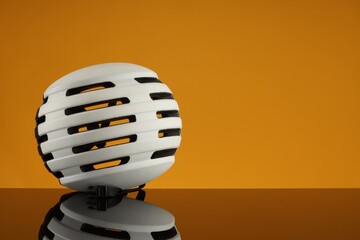 White protective helmet on mirror surface against orange background. Space for text