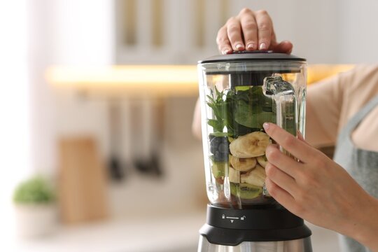 Woman making delicious smoothie with blender in kitchen, closeup
