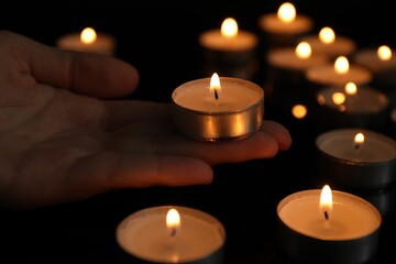Woman holding burning tealight candle on black background, closeup