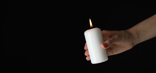 Woman holding burning candle on black background, closeup. Space for text. Banner design