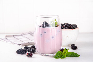 Mulberry shake, smoothie or yogurt drink on portioned glass, with a lot of fresh organic mulberry berries and mint, on white kitchen table, copy space