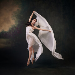 Fototapeta premium Draped in delicate fabric, dancer embodies lightness and fluidity in her movements against vintage studio background. Concept of ballet, history, fusion of modernity and ancient times in art.