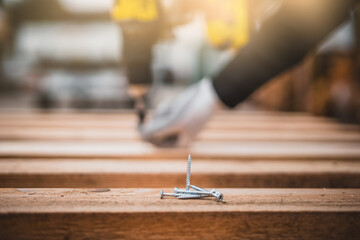 Close up man hand holding electric cordless screwdriver machine and screws lie for screwing a screw assembling wood construction. Iron screw, screws as a background, wood screw, concept industry.