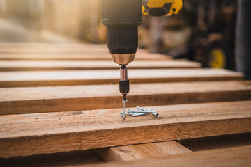 Close up man hand holding electric cordless screwdriver machine and screws lie for screwing a screw assembling wood construction. Iron screw, screws as a background, wood screw, concept industry.