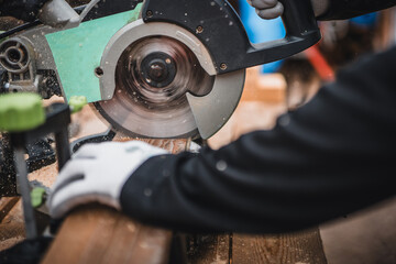 Working on a circular saw in a workshop. Male muscular hands lower the handle and blade of a miter saw to cut off the edge of a wooden fillet.