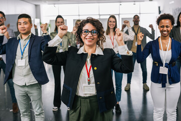 Fototapeta premium Portrait of Hispanic woman CEO standing in front of her multiracial colleagues with their hands in the air, celebrating their success.
