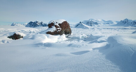 Snowy winter arctic landscape in sunny day. Desert white land of snow and ice, snow-covered mountains in the background. Breathtaking journey over frozen Antarctica landscape. Low angle drone shot