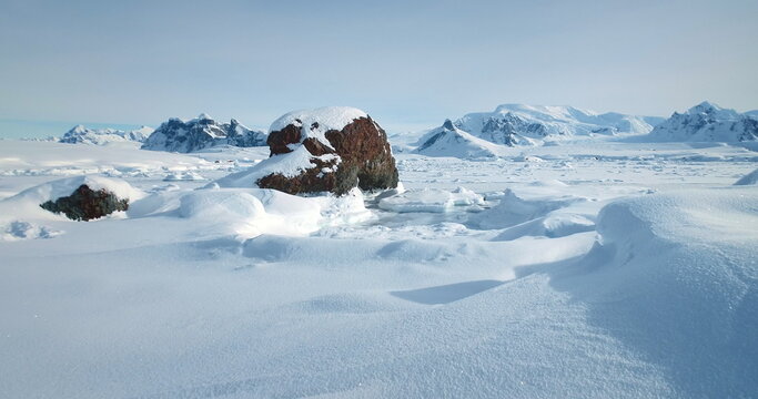 Snowy winter arctic landscape in sunny day. Desert white land of snow and ice, snow-covered mountains in the background. Breathtaking journey over frozen Antarctica landscape. Low angle drone shot