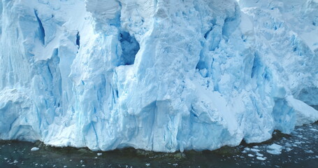 Obraz premium Giant glacier towering in Antarctica polar ocean. A huge iceberg ice wall formation float cold water, mountain slope in background. Winter landscape close up. Climate change at polar glacier landscape