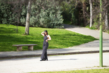 Fototapeta premium Young and beautiful woman, brunette and black dress with white polka dots posing for a photo shoot on the road, the woman is wearing make-up and red lipstick.
