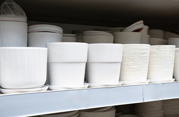 A neat row of white ceramic plant pot on the rack shelves. Different shapes and design. For sale. Fragile and handle with care. Concept of neat, peaceful, hobby, collection and gardening. Malaysia