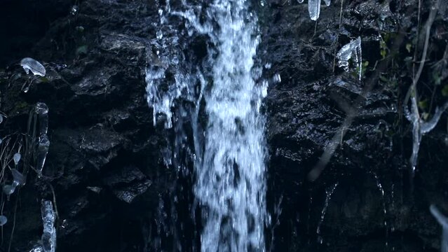 acqua che scorre lungo una piccola cascata in roccia, all'ombra, in un ambiente naturale in montagna, in un'atmosfera fredda con tonalit&agrave; di azzurro