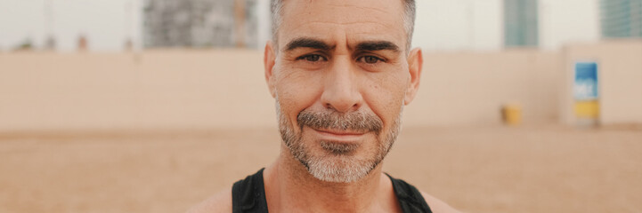 Close up, middle aged athletic man smiling and looking at camera while standing on the beach