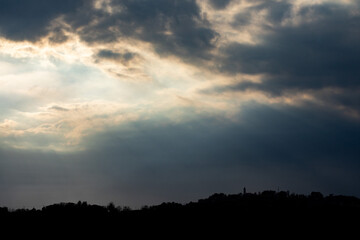 raggi di luce solare che passano attraverso le nuvole, di pomeriggio ed evidenziano le sagome scure delle colline 