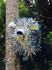 Creative recycled tire sculpture resembling a white puffer fish attached to a tree in an outdoor...