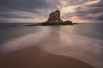 Cloudy sunrise on Camello beach, Santander, with water, sand and rocks in the foreground