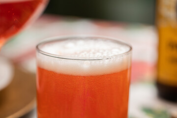 vista in primo piano di un bicchiere trasparente messo su un tavolo apparecchiato, riempito completamente con una bevanda dolce, gassata e frizzante di colore rosso