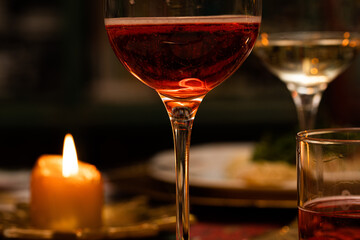 dettagli macro di un calice su un tavolo, riempito con una bevanda rossa, vicino ad altri bicchieri, piatti e una candela accesa