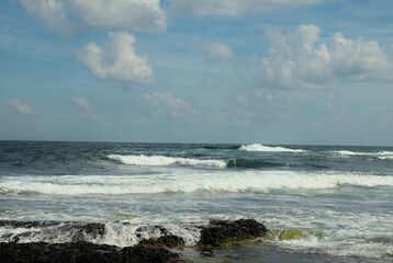 A stormy sea with waves rising and crashing against a rocky shore. Clear day with a blue sky. Background.