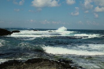 A stormy sea with waves rising and crashing against a rocky shore. Clear day with a blue sky. Background.