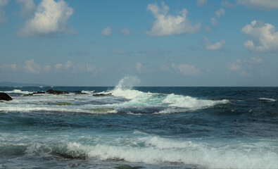 A stormy sea with waves rising and crashing against a rocky shore. Clear day with a blue sky. Background.