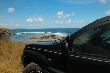 A jeep on a hill overlooking the sea and cliffs on a clear sunny day. On an adventure-filled journey by car.