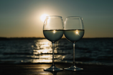 Two glasses of wine on wooden table near river at sunset