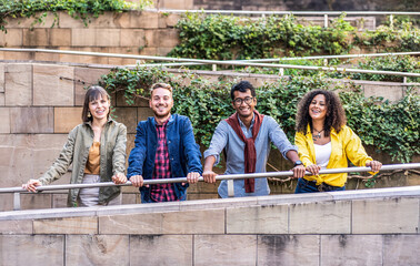 Generation Z friends smiling and standing by a railing outdoors. A diverse group of young adults enjoying each other's company in a natural urban setting.