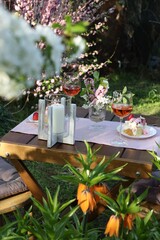 Vase with spring flowers, wine and cake on table served for romantic date in garden