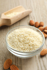 Fresh almond flour in bowl and nuts on wooden table, closeup