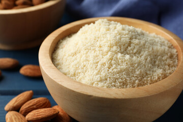 Fresh almond flour in bowl and nuts on blue table, closeup