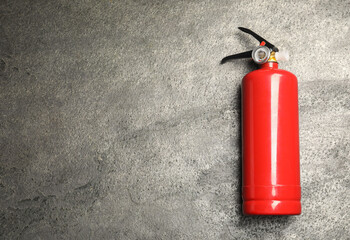 Fototapeta premium One red fire extinguisher on gray textured background, top view. Space for text