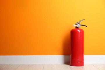 Fototapeta premium Fire extinguisher on floor near orange wall, space for text