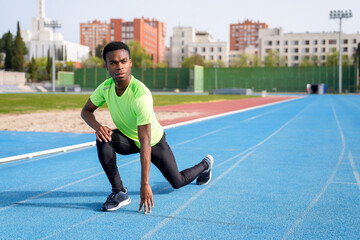 A african man in a green shirt is stretching on a track