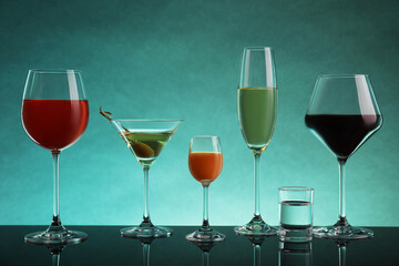 Glasses with different alcoholic drinks on table against turquoise background