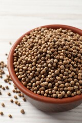 Dried coriander seeds in bowl on wooden table, closeup